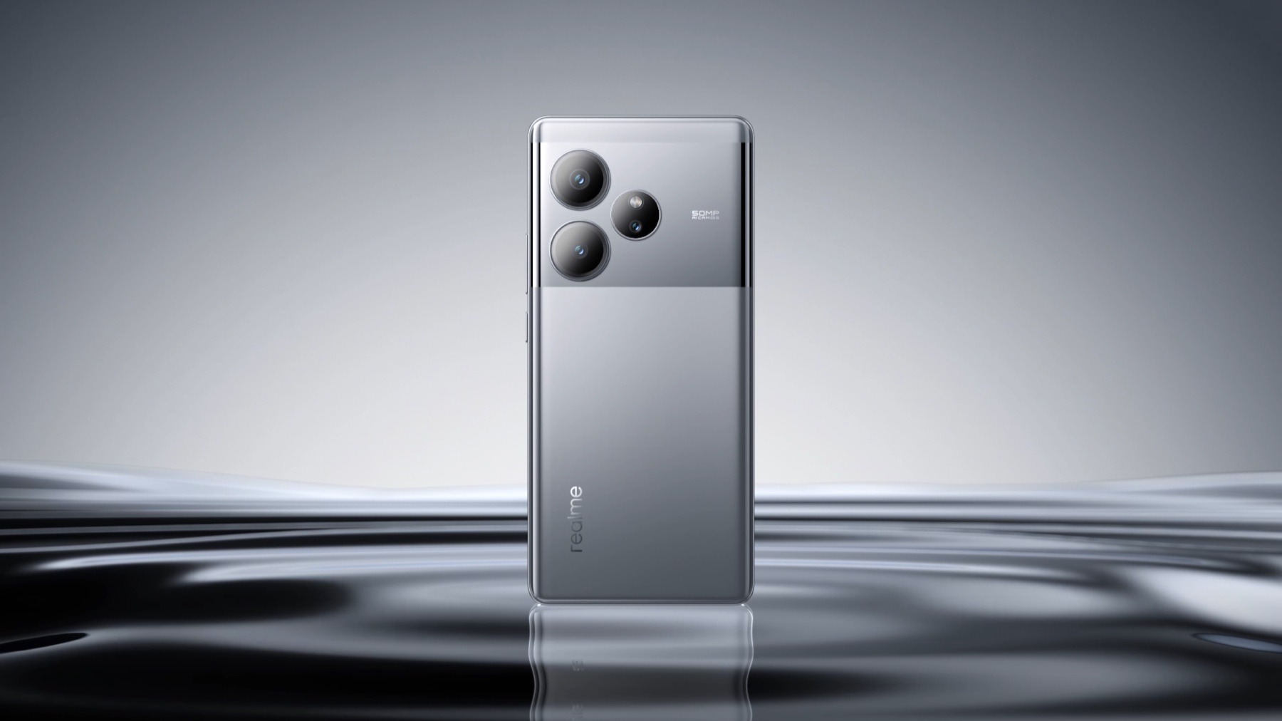 realme GT 6 in Fluid Silver, back panel and triple camera module, standing upright on a reflective studio surface